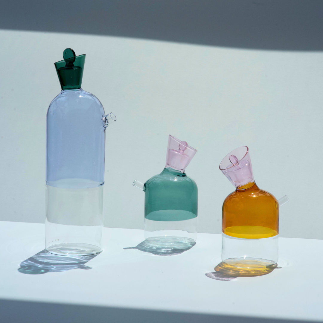 Set of three colorful glass bottles with different shapes on a white surface.