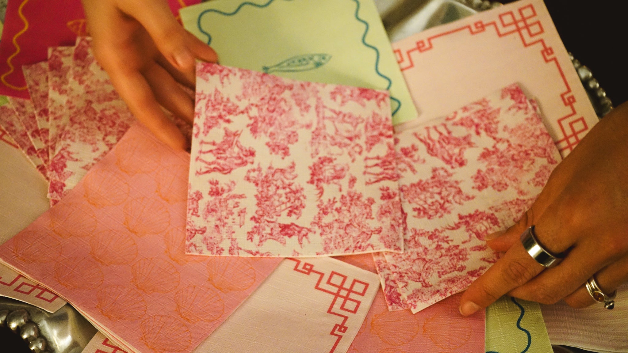Hands holding a piece of red and white patterned paper among other colorful napkins.