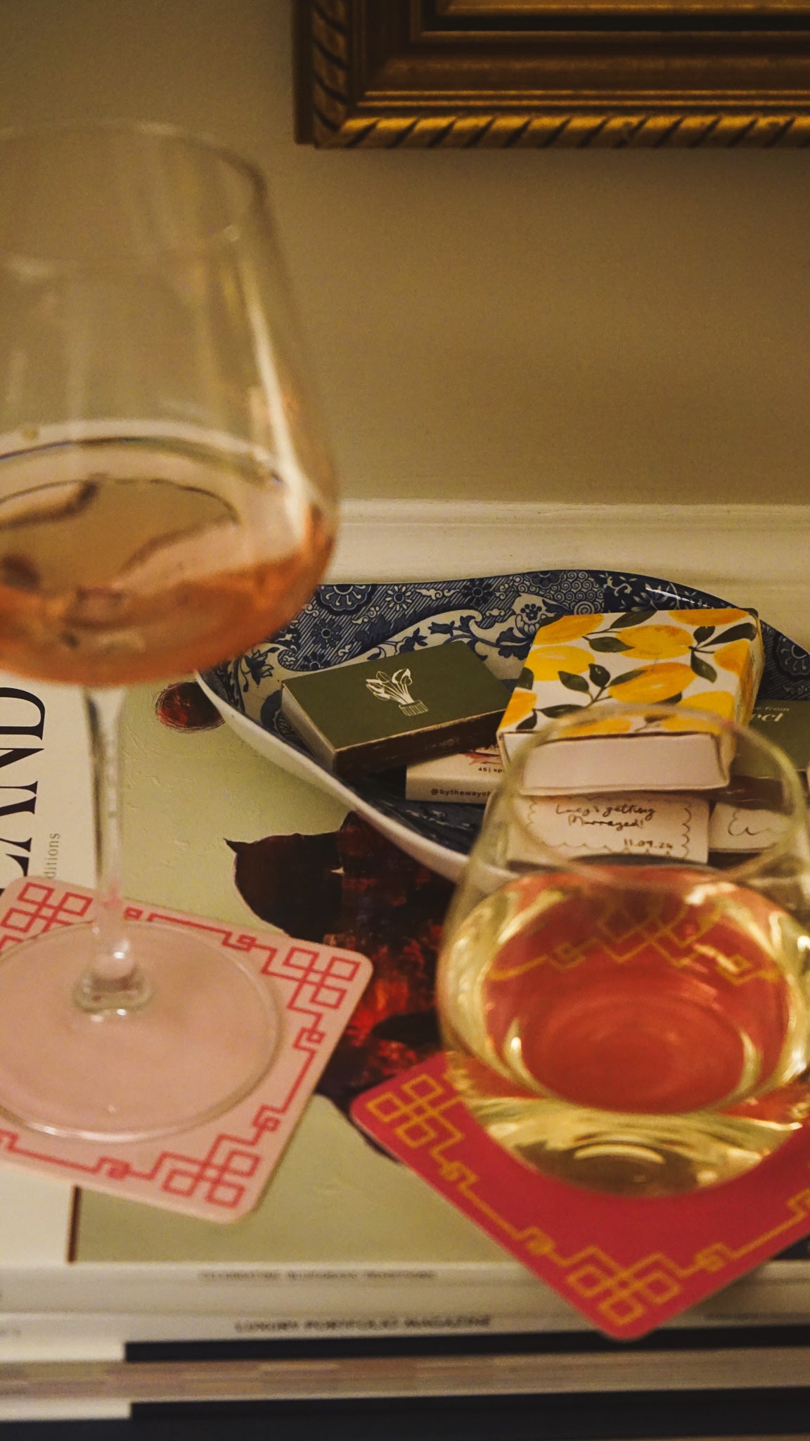 Two wine glasses with red wine on a decorative surface with books and a framed picture.