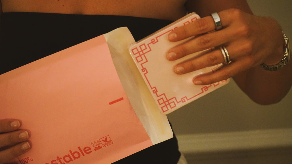 Person holding a pink envelope with a brand logo, wearing rings on their fingers.