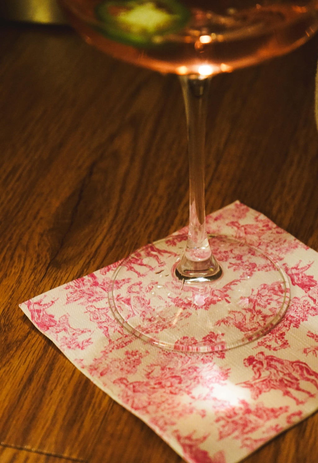 Wine glass with pink liquid on a decorative napkin on a wooden surface.