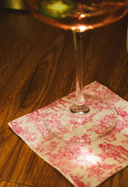 Wine glass with pink liquid on a decorative napkin on a wooden surface.