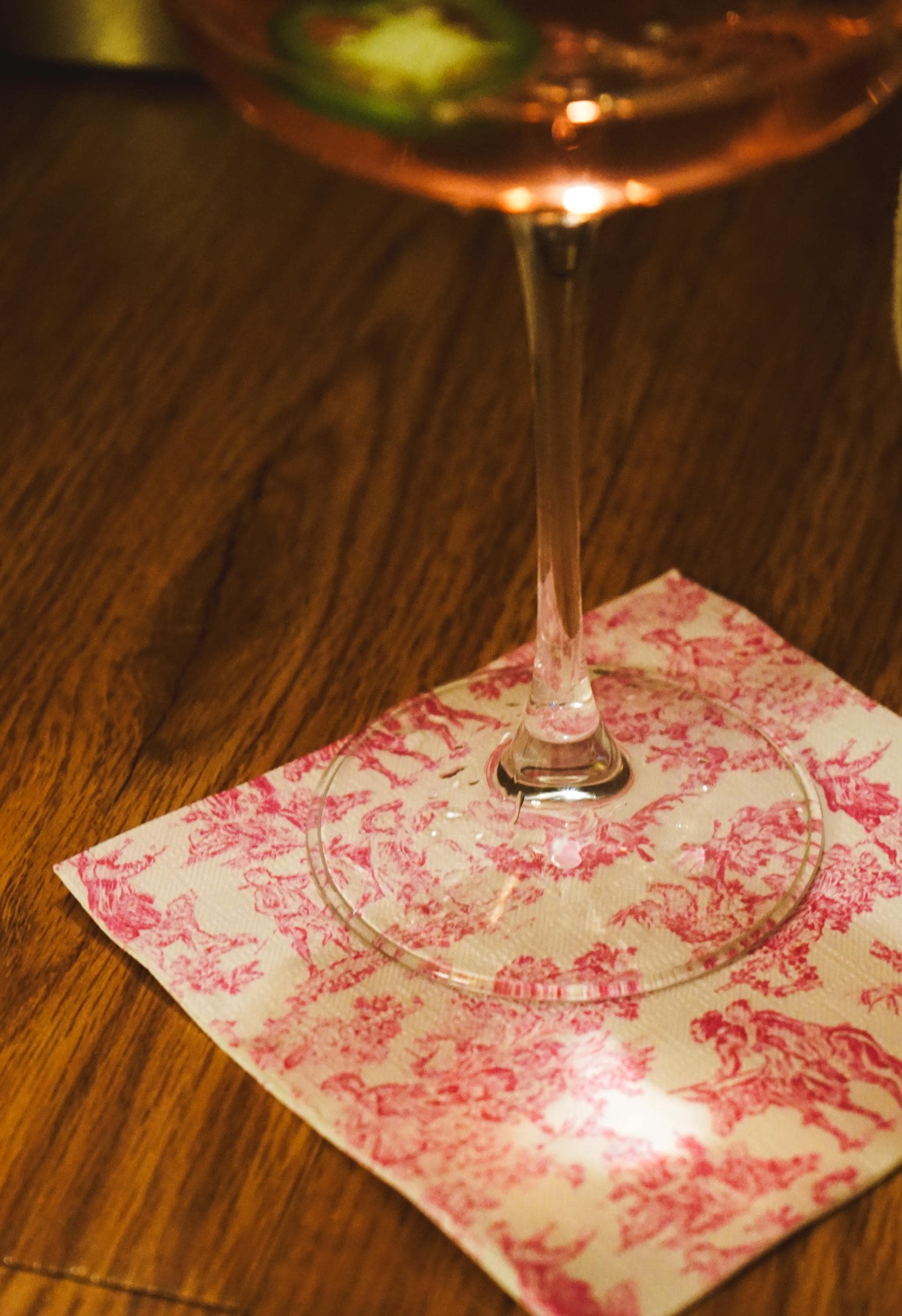 Wine glass with pink liquid on a decorative napkin on a wooden surface.