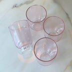 Four pink-rimmed glass tumblers on a marble surface